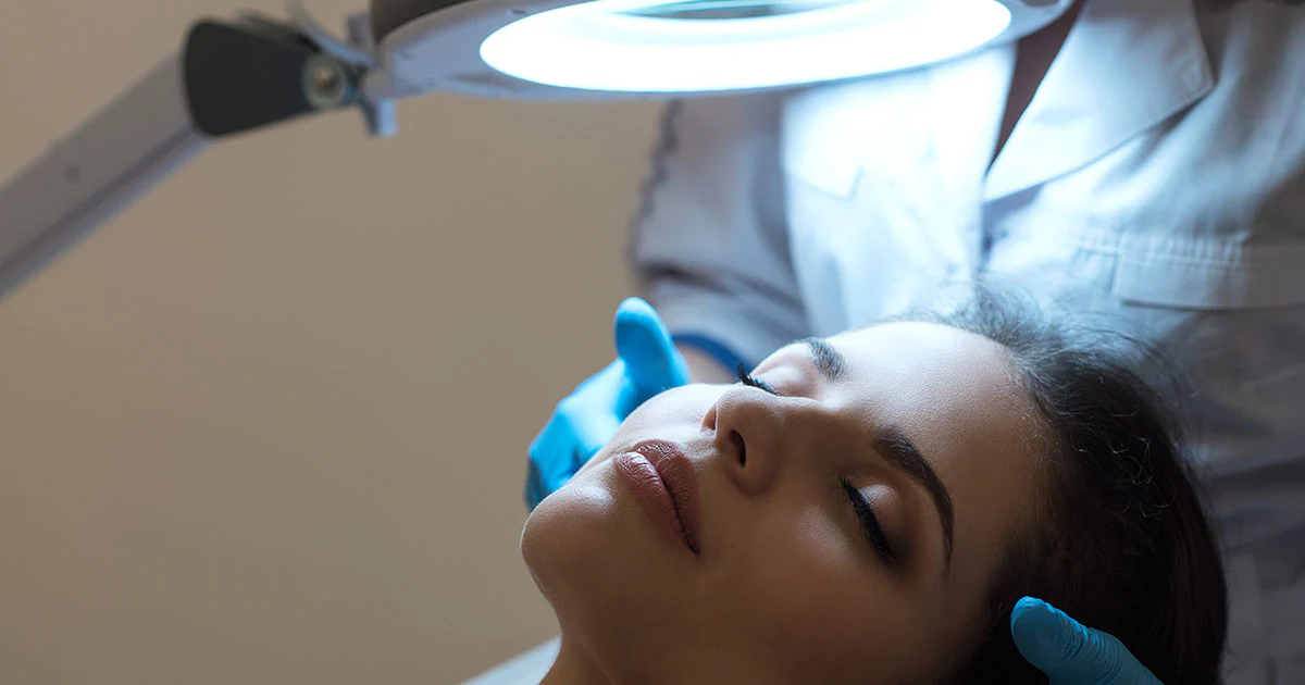 A dermal clinician examining a client's skin under a magnifying lamp